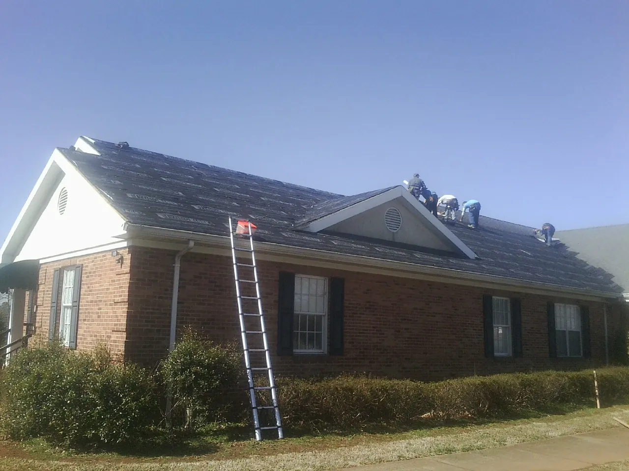 Crew tearing shingles off a brick ranch roof with a ladder set — Emergency Roof Repair work by our crew in Manquin