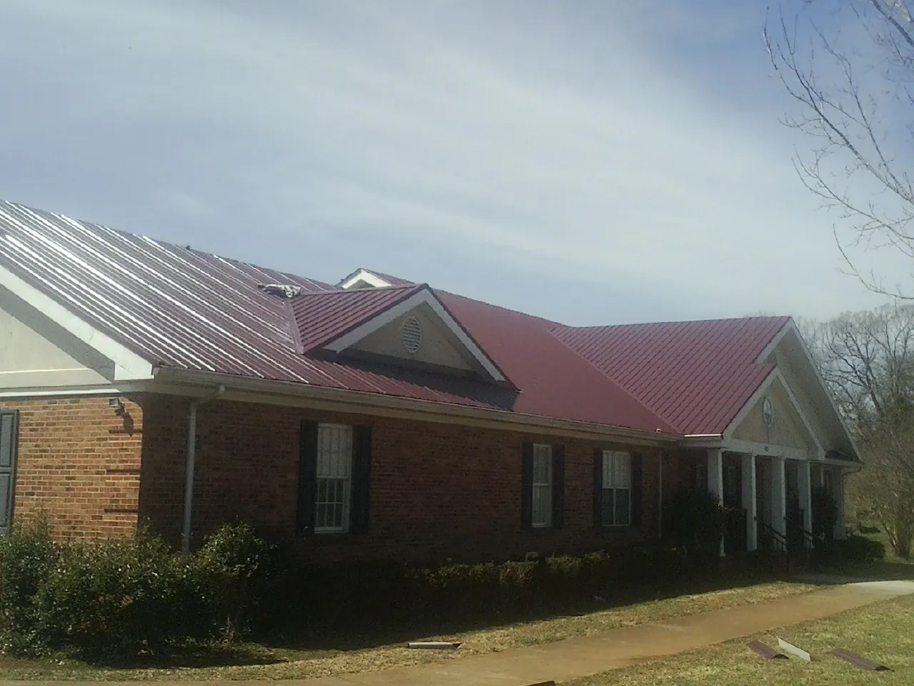 Red metal roof with gabled entries on a long brick building, from a Hail Damage Roof Repair job in Manquin