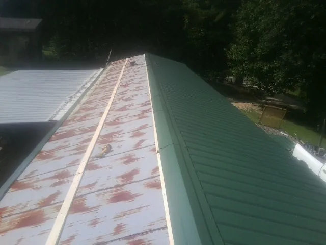 Old rusted panels beside newly installed green metal roofing — Wind Damage Roof Repair by Roofing Brothers in Manquin