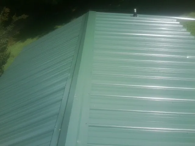 New green metal panels meeting at the ridge of a roof — Flat Roof Repair work by our crew in Manquin