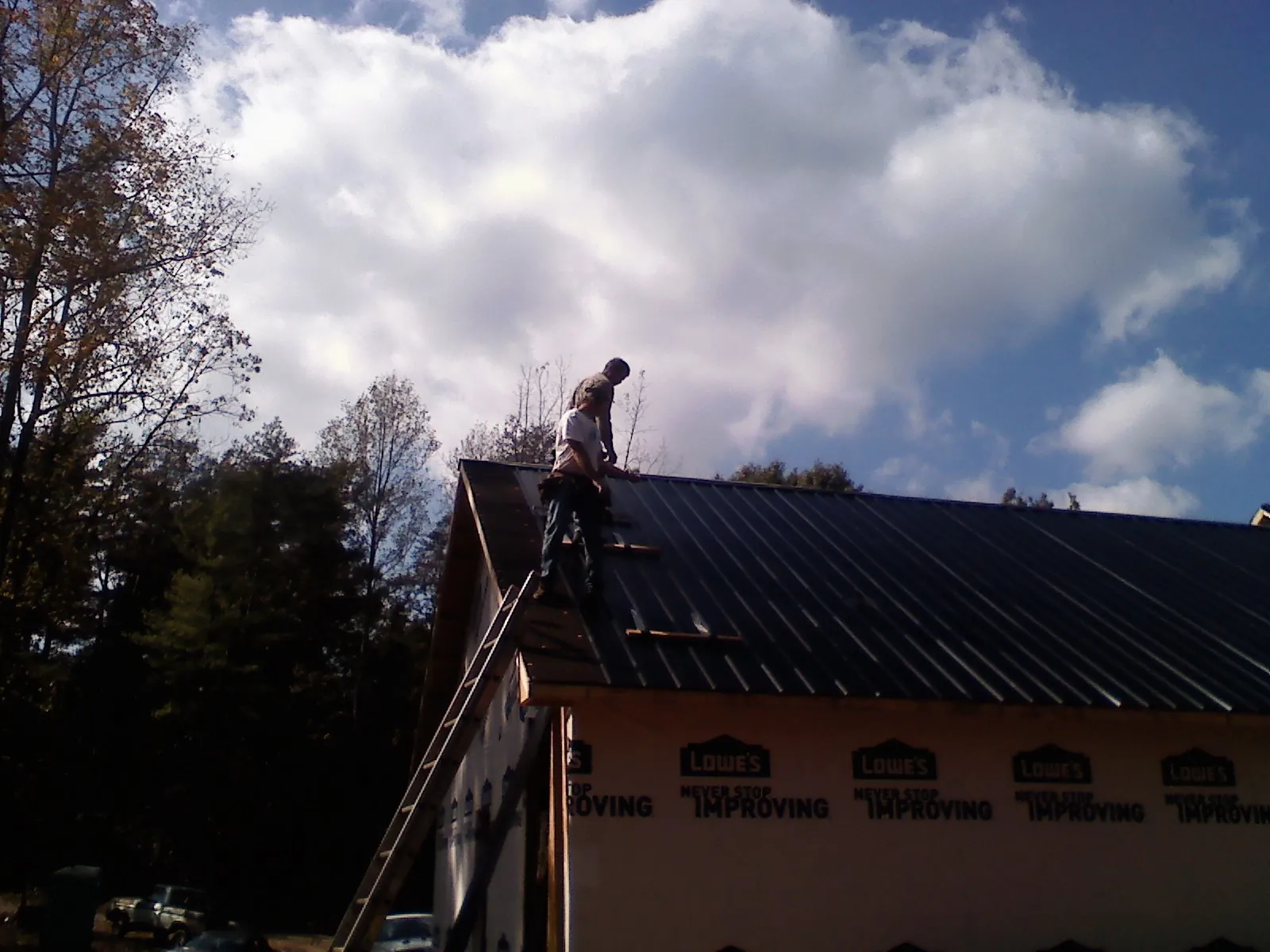 Roofer fastening dark metal panels high against a cloudy sky, from a Roof Inspection job in Manquin
